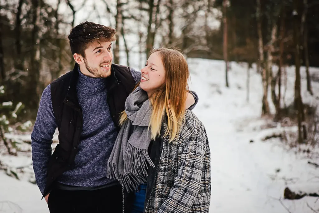 Ein lachendes Paar in Winterkleidung spaziert im verschneiten Wald. Fotografie von Daniel Spiehs.